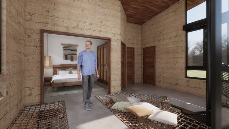 A man walking into a rustic bedroom with wood-paneled walls, a bed with a wooden headboard, decorative pillows and a tapestry hanging above, and open wardrobe doors, with large windows showing an outdoor view.