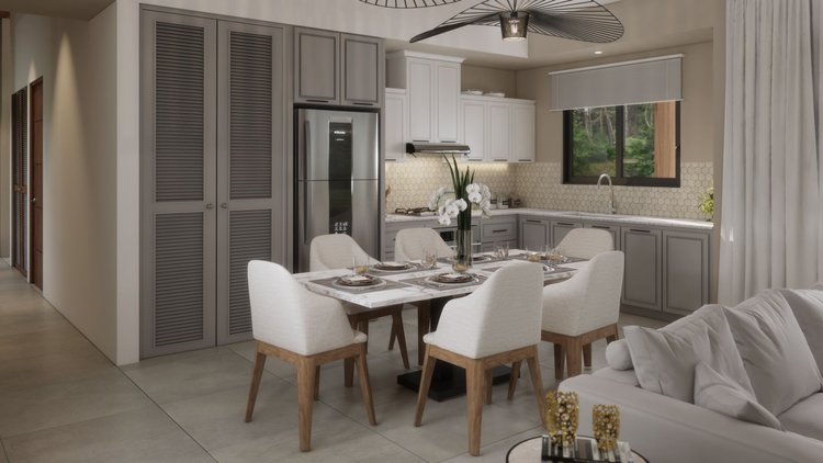 Dining area with a marble table set with plates, glasses, and white napkins, surrounded by eight upholstered chairs, nearby is a sofa with pillows, in an open kitchen with gray cabinets, stainless steel refrigerator, window, and modern lighting.