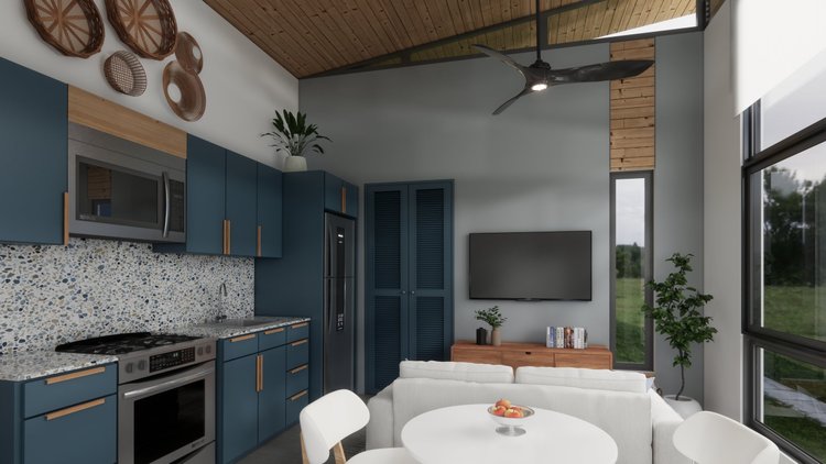 Modern living room with blue kitchen cabinets, a TV, and a white sofa. Large windows with a view of greenery outside, wooden ceiling and decor, including woven baskets on the wall, houseplants, and a dining table with a bowl of peaches.
