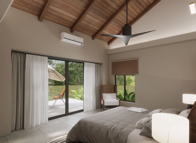 A bedroom with a bed, pillows, and a bedside lamp. It has large glass sliding doors opening to a patio with an outdoor lounge chair and umbrella, and a window with a wooden blind. The ceiling is wooden with exposed beams, a modern ceiling fan, and an