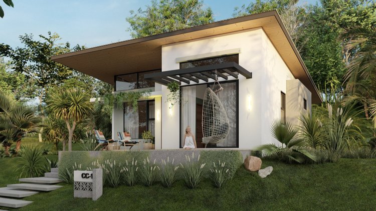Modern house with a white exterior, large glass windows, and outdoor patio with chairs, surrounded by lush green plants and trees, a woman sitting on the patio near a hanging chair.
