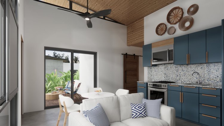 Modern kitchen and living area with blue cabinets, a patterned backsplash, white sofa with blue and white pillows, and a sliding glass door leading to a patio with outdoor chairs and greenery.